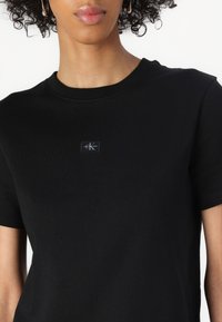 Svart bomull T-skjorte med rund hals og korte ermer. Har et lite, rektangulært logo-glepp på brystet. Glatt tekstur.