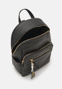 Mochila negra de cuero con forma redondeada, cremalleras doradas, dos bolsillos frontales y un llavero decorativo. Exterior texturizado con un interior suave.
