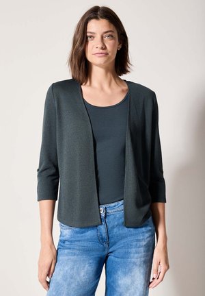 Cardigan vert foncé avec une texture légère, ouvert à l'avant et à manches trois-quarts, porté par-dessus un débardeur noir et un jean bleu clair.
