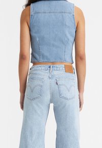 Ljusblå denimbestämd cropped vest med rak fåll och utan ärmar, som matchas med högmidjade ljusblå vida jeans med bakfickor.