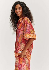 Farebná krátkoplejá košeľa s patchwork paisley vzormi v odtieňoch červenej, oranžovej a ružovej. Ľahká tkanina s uvoľneným strihom.