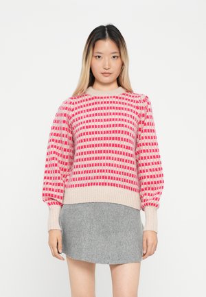 Pull en tricot rose clair avec des motifs géométriques rouges, doté de poignets et d'un ourlet côtelés. Associé à une jupe grise.