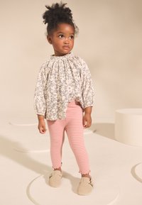 Blouse fluide crème avec motif floral bleu, encolure froncée ; leggings à rayures roses ; chaussures souples beiges avec détail boucle.