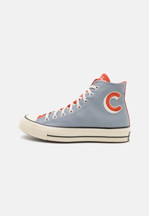 Højtop-sneaker i lyseblåt lærred med hvide snørebånd, rød inderforing, rød "C"-logo på siden og cremefarvet gummisål med sorte striber.