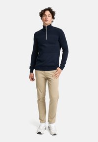 Marineblauer Strickpullover mit Viertelreißverschluss und strukturiertem Muster, kombiniert mit beigen Chinos und weißen Sneakers, präsentiert einen eleganten, modernen Freizeitlook.