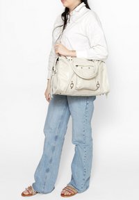 Sac à main gris clair en tissu doux, doté d'une poignée tressée, d'une fermeture éclair et d'accents métalliques. Design structuré avec des coutures visibles.