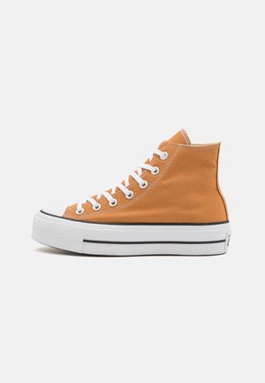 Sneaker montante en toile orange avec lacets blancs, semelle en caoutchouc blanche et détail bande noire sur le côté.