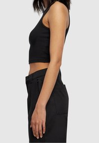 Svart randig croptopp med en figurnära design, utan ärmar och mjukt material, kombinerad med högmidjade svarta byxor med sidofickor.