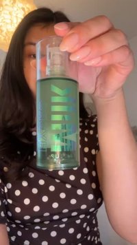 Green spray bottle with a clear top. Features iridescent lettering and a pump. Notable for its round shape and glossy finish.