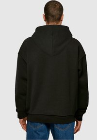 Svart oversized hoodie med en rymlig huva, ribbade muddar och nederkant. Tillverkad av mjukt tyg, visar upp en minimalistisk design utan synliga logotyper.