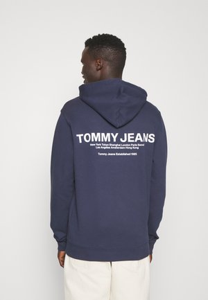 Felpa blu navy con tasca a marsupio, caratterizzata dal logo bianco "TOMMY JEANS" e nomi di città stampati sul retro. Tessuto morbido in misto cotone.
