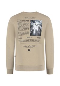 Beige sweatshirt met zwarte tekst en een afbeelding van haaien die boven stedelijke wolkenkrabbers vliegen, met zinnen over de natuur en het stadsleven.