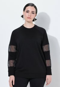 Felpa nera con maniche lunghe, caratterizzata da pannelli in rete trasparente sulle braccia. Collo a giro e vestibilità comoda, realizzata in tessuto morbido.
