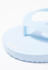 Sinine rannauss, millel on sujuv, matta tekstuur, õhuke tekstureeritud rihm ja laineline servadisain taldadel. Kuldne logo detail on kaasas.