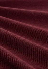 Nahaufnahme von gefaltetem, dunkelrotem, strukturiertem Stoff mit einem Waffelmuster.