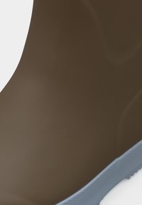 Καφέ λαστιχένια μπότες με λείο φινίρισμα και ανοιχτό μπλε σόλα. Διαθέτουν στρογγυλεμένη πάνω άκρη και υφή στη σόλα.