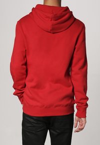 Roter Pullover-Hoodie aus weichem Stoff. Verfügt über eine große Kapuze, gerippte Bündchen und Saum. Schlichtes Design ohne sichtbare Muster oder Akzente.
