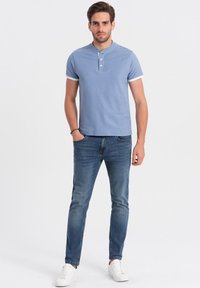 Světle modré polo tričko s henley výstřihem a třemi knoflíky, spárované s tmavě modrými džíny a bílými teniskami. Hladká tkanina, volný střih.