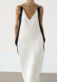 Ærmeløs kjole i hvid og sort, lavet af hør. Har en V-udskæring, brede sidelommer og kontrasterende stropper. Rent, minimalistisk design.