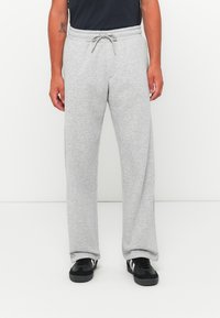 Mann iført lysegrå joggebukser med snor i livet og svarte joggesko med hvit stripe, stående foran hvit bakgrunn.