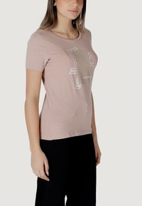 Camiseta de manga corta rosa claro en tejido suave, con un diseño gráfico en plateado, cuello redondo y cuerpo ajustado.