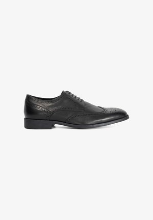 Chaussure brogue pour hommes en cuir noir avec design à embout ailé, détails perforés et talon bas, vue de côté sur un fond blanc.