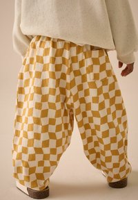 Hosen im Schachbrettmuster in Gelb und Weiß, aus strukturiertem Stoff gefertigt. Mit elastischem Bund und Seitentaschen.