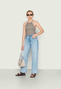 Top halter em padrão gingham preto e branco, calças de cintura alta e pernas largas em azul claro, sandálias pretas e uma pequena bolsa bege com alça de corrente.
