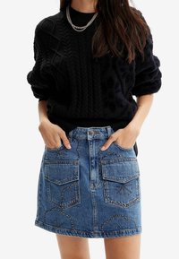 Černý svetr s kabelovým vzorem a ohrnutými rukávy v kombinaci s džínovou minisukní se dvěma předními kapsami a dekorativními cvoky.