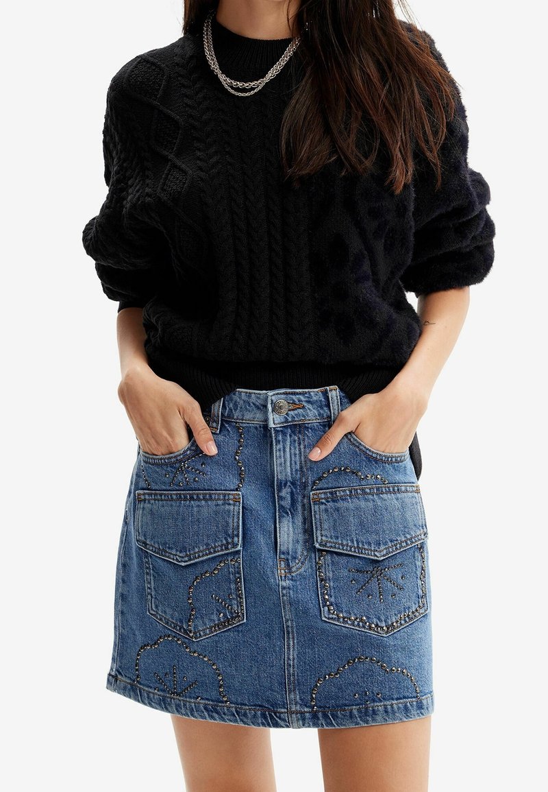 Černý svetr s kabelovým vzorem a ohrnutými rukávy v kombinaci s džínovou minisukní se dvěma předními kapsami a dekorativními cvoky.