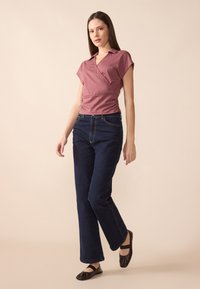 Rosa-farget kortermet omslagstopp med krage, paret med mørkeblå rette jeans og svarte flate sko. Glatte teksturer på stoffet.