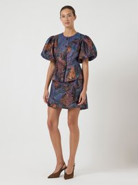 Ανάλαφρο πολύχρωμο φόρεμα με φουσκωτά μανίκια, που διαθέτει μια υφασμάτινη αφηρημένη μοτίβο σε αποχρώσεις μπλε, μωβ και πορτοκαλί, κλείνει με κουμπιά.