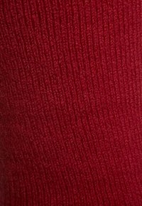 Κόκκινο πλεκτό ύφασμα με ραβδωτή υφή, που διαθέτει επιμηκυμένες κάθετες γραμμές και εμφανίζει μια απαλή, ζεστή όψη.