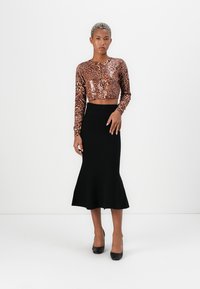 Cropped leopard print long-sleeve top with a button closure, paired with a black fishtail midi skirt. Worn with black high-heeled shoes.