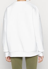 Bílá mikina se volným střihem, žebrovanými manžetami a lemem, s postranním zipem a hladkou, jemnou texturou látky.