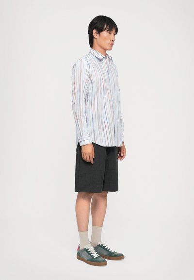 Chemise à rayures bleu clair, avec des lignes verticales rouges et oranges ; assortie à un short foncé et des baskets multicolores.