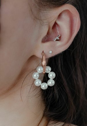 Kupfer-Hoops mit zwölf strahlend weißen Perlen, neben einem kleinen Steckerohrring am Ohr platziert. Glatte Textur.