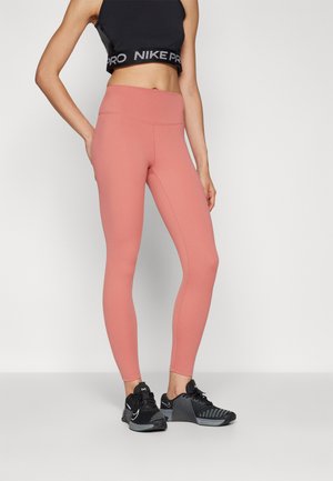 Nike Pro High-Waist-Leggings in zarter Koralle, mit einer glatten Textur und passgenauem Design, kombiniert mit schwarzen Sportschuhen.