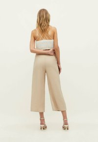 Top court en crochet blanc avec des bretelles spaghetti ; pantalon beige à jambes larges avec une texture ; modèle portant des talons beiges à lanières.