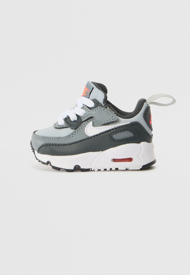 Gyerek Nike sneakers szürke és fehér színben. Jellemzői közé tartozik a szövet és szintetikus felsőrész, fűzők, kontrasztos sarokfül, valamint piros részletek.
