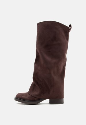 Hoher brauner Wildlederstiefel mit niedrigem Blockabsatz und einer Zuglasche hinten, seitlich auf hellem Hintergrund gezeigt.