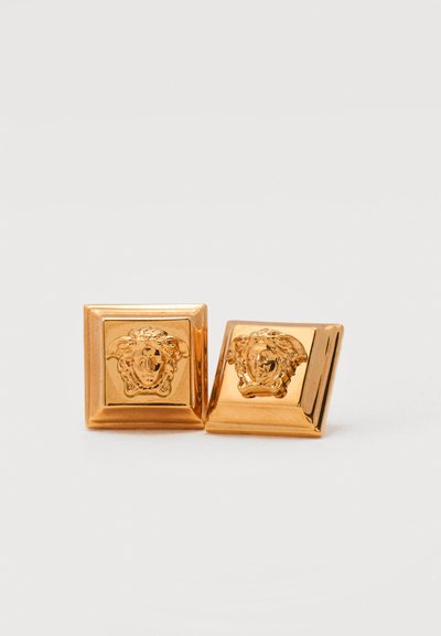 Χρυσά τετράγωνα μανικετόκουμπα με ανάγλυφο σχέδιο κεφαλής Μέδουσας, γυαλιστερό φινίρισμα, τοποθετημένα σε απλό φωτεινό φόντο.