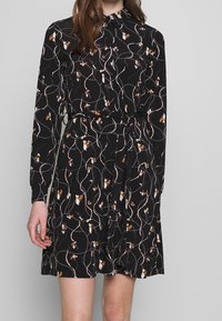 Black dress with long sleeves, floral print in white and orange, fitted waist with a belt, soft texture, and curved hemline.
