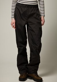 Černé outdoorové kalhoty s elastickým pasem, lehkým materiálem, zúženými nohavicemi a precizním šitím; nošeny s hnědými turistickými botami.