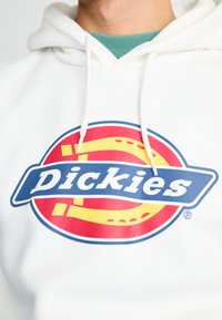 White hoodie featuring a large circular logo with red and yellow elements and blue text reading "Dickies." Thick drawstrings present.