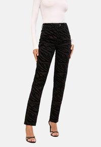 Mustad corduroy püksid, millel on tõstetud musta tiigri triibud, sirge lõige ja viie taskuga disain, koos rihmadega kontsakingadega.