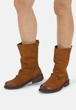 Mid-calf brown leather boots with darker toe caps and low wooden heels worn on bare legs against a plain background.