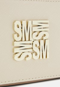 Bežna torba s teksturiranom površinom i metalik zlatnim grbom s natpisom "SM" složenim u podebljanom, modernom fontu.