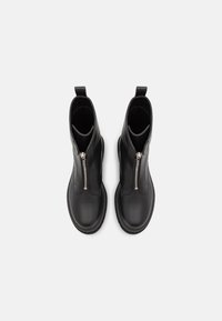 Botines de cuero negro con acabado liso, que cuentan con una cremallera central, pestañas de agarre en forma de lazo y puntera redondeada. Suela plana con detalles de costura.