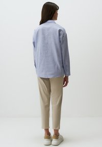 Blauw-wit gestreepte shirt met een relaxte pasvorm en knoopmanchetten, gecombineerd met beige tapering broek en witte sneakers.
